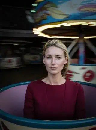 Army Dreamers AI trend: a woman in a dark red top sits in a spinning teacup ride under blurred fairground lights