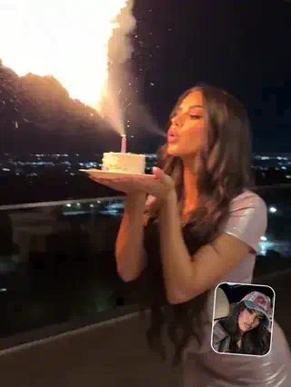 Woman on a night rooftop blowing on a birthday candle as a big plume of fire shoots up from the cake