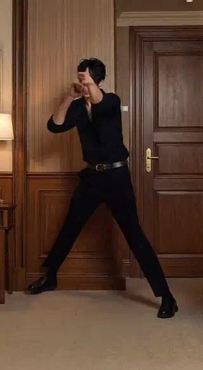 AI dance video: a man in black dances with one hand at his face in a wood-paneled room